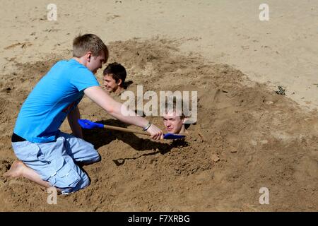 A boy buries two others up to their necks in the sand! Stock Photo