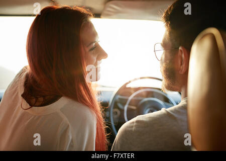 Rear view of happy young couple on a road trip on a summer day. Affectionate young couple on vacation travelling by their car. Stock Photo