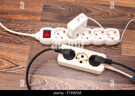 Many plugs plugged into electric power bars on floor Stock Photo