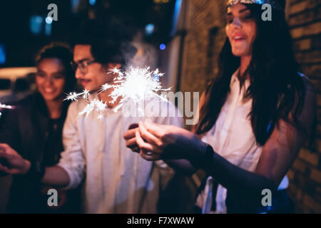 Young friends out at night, celebrating with sparklers. Men and women hanging out at night having a party. Stock Photo