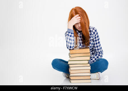 Sleepy sad redhead young lady leaning on stack of books and having a headache over white background Stock Photo