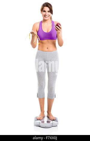 Beautiful athletic woman over a scale and holding an apple and a measure tape, isolated over white background Stock Photo