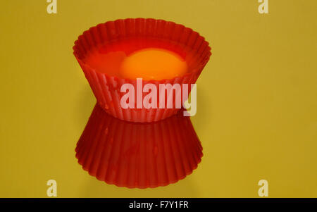 Raw egg in red plastic baking muffin cup and reflection onyellow background Stock Photo