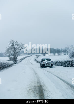 A 4x4 Land Rover vehicle drives through hazardous deep snow and ice on a remote country road in Monkton Farleigh, Wiltshire, UK Stock Photo