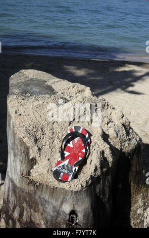 A single sandal with a GB UK Union Jack Flag design found resting on a sand covered tree stump on the beach in Pattaya Thailand Stock Photo