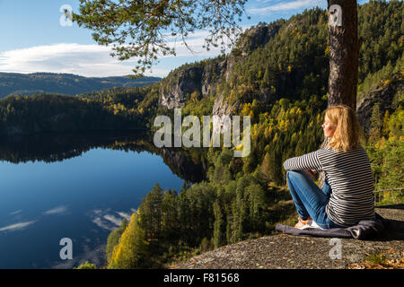 Beautiful young woman contemplating nature on top of a cliff overlooking a beautiful lake Stock Photo