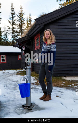 Pretty girl filling a bucket using a hand pump from a well outside a cabin in the forest North of Oslo - portrait Stock Photo