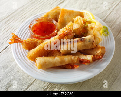 Cooked mixed Chinese starters - Dim sum, breaded prawns, spring rolls with chilli sauce served on a white plate