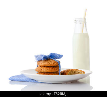 Stack of three homemade oatmeal cookies tied and bitten cookie on white ceramic plate and bottle of milk Stock Photo