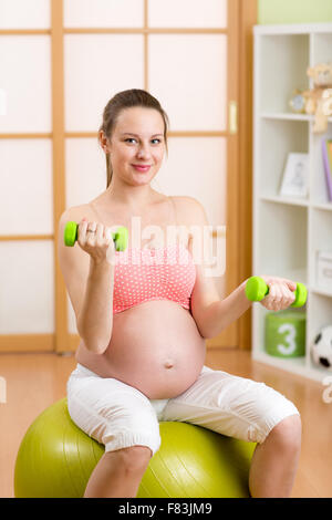 Pregnant woman doing fitness exercises sitting on a gym ball with dumbbells Stock Photo