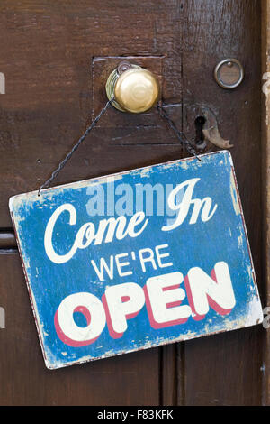 Sign "Come in we're open" hanging on a wooden door Stock Photo