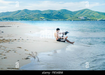 A Caucasian man prepares to put on swim fins prior to snorkeling in the Caribbean, on Turtle Beach, Buck Island, U.S.V.I. USVI. St. Croix background. Stock Photo