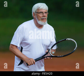 Senior man playing tennis on a gravel court Stock Photo