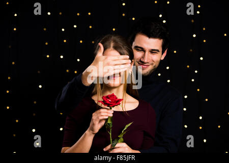 young couple, man and woman, on black background, man is presenting a rose, covering womans eyes Stock Photo