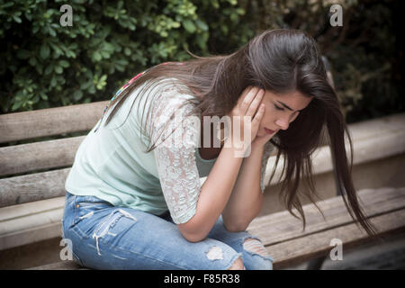 Stressed young woman sat on bench head in hands Stock Photo