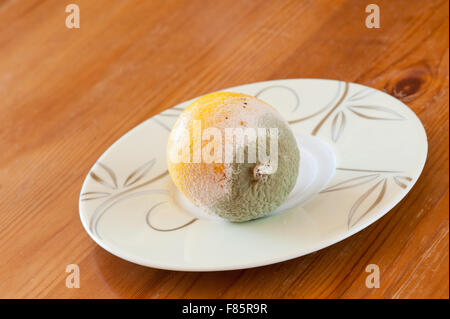 Mouldy yellow lemon fruit lying on small plate on wooden table, moldy and decayed bad food wastage, one lemon garbage horizontal Stock Photo