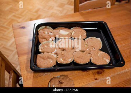 Spilled out muffins cupcakes in paper pan liners lying on black baking tray on table, many sweet treats with apples spilled out Stock Photo
