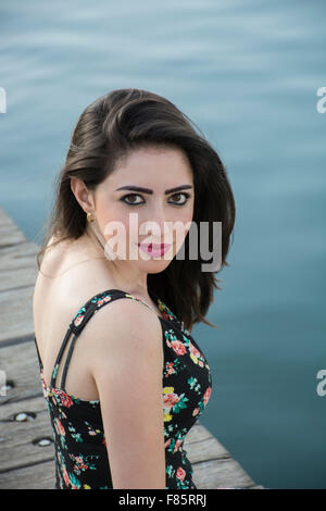 Beautiful young woman sat on the pier smiling Stock Photo