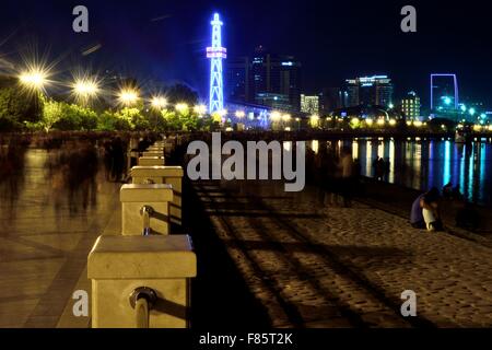 Baku Bulvar at night with people blurred due to movement, reflections on the Caspian Sea and buildings lit up brightly Stock Photo