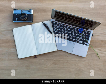 Laptop, opened notepad laptop, and vintage film camera lying on a wooden table. Stock Photo