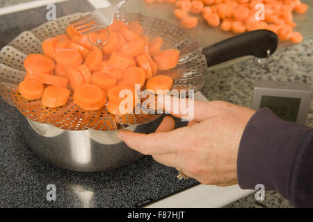 Pulling expandable strainer out of pot where carrots were being blanched in preparation for blanching Stock Photo