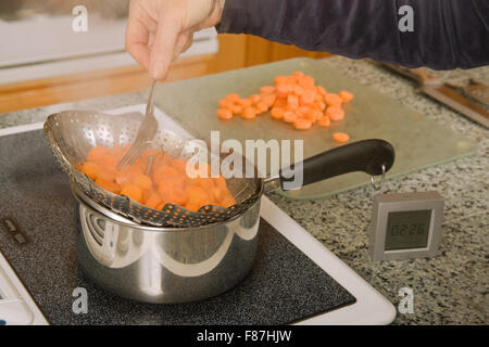 Pulling expandable strainer out of pot where carrots were being blanched in preparation for blanching Stock Photo