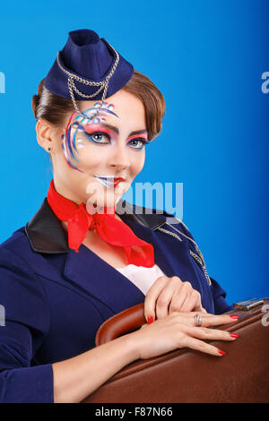 Stewardess with face art holds suitcase. Young attractive girl in a blue suit flight attendants. Air services. Service. Baggage. Stock Photo