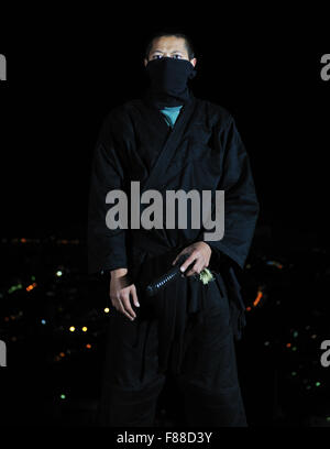 ninja assasin hold katana samurai old martial weapon swordat night with city lights in background Stock Photo