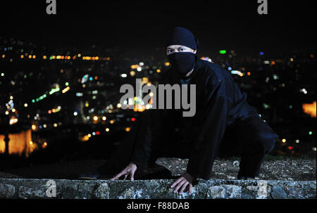 ninja assasin hold katana samurai old martial weapon swordat night with city lights in background Stock Photo