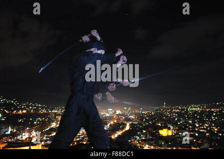 ninja assasin hold katana samurai old martial weapon swordat night with city lights in background Stock Photo