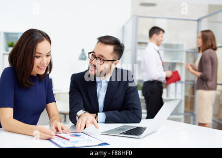 Two colleagues discussing document in working environment in office Stock Photo