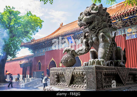 Lion statue at Lama Temple in Beijing with people worshiping in the background and  smoke rising Stock Photo