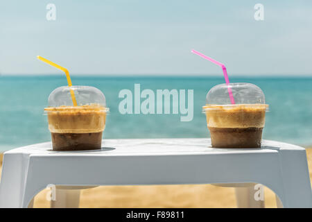Two ice frappe coffee on white plastic coffee table in plastic transparent cups, with yellow and magenta straws, on summer day. Stock Photo