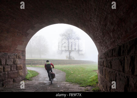 Cyclist cycling on a cycle path and emerging from under the arch of a bridge on a foggy day in Autumn, Nottinghamshire, England, UK Stock Photo