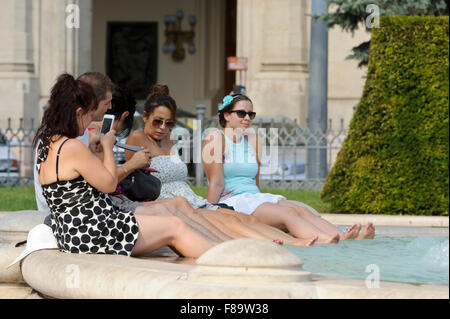 A group of young women sitting on the edge of a water fountain with their feet soaking in the cold water, Budapest, Hungary. Stock Photo