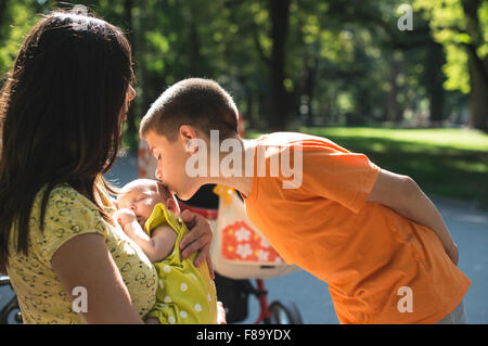 Women, brother and baby in a park. Child kissing baby Stock Photo