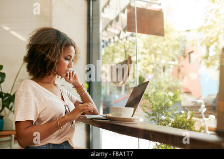 Young black female at cafe using laptop. African young woman sitting in a restaurant busy working on her laptop. Stock Photo