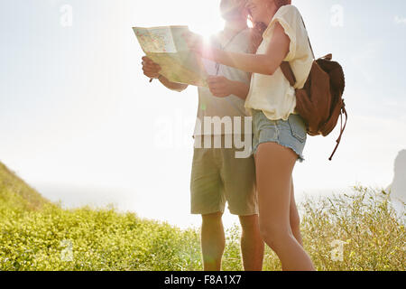 Young couple looking at map while standing outdoors in countryside with bright sunshine from behind. Couple looking for directio Stock Photo