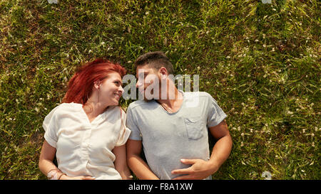 Overhead view of happy young couple in love relaxing on the grass. Affectionate young man and woman lying on grass looking at ea
