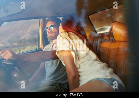 Woman kissing man driving car. Couple on road trip. Romantic caucasian couple on holiday having fun in car. Stock Photo