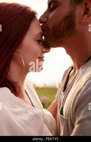 Portrait of loving young couple together outdoors. Young man kissing forehead of his girlfriend. Stock Photo