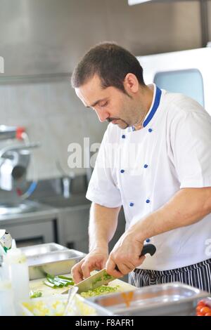 Handsome chef dressed in white uniform decorating pasta salad and seafood fish in modern kitchen Stock Photo