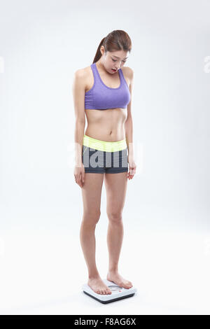 Woman in sportswear standing on a scale and looking down Stock Photo