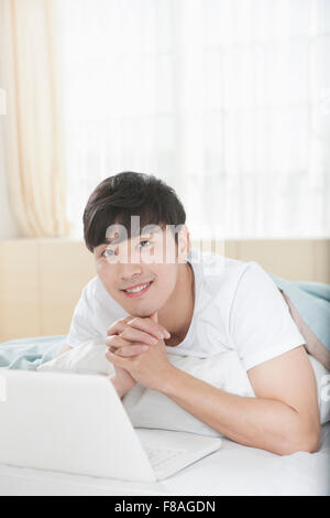 Man lying on his stomach on bed with computer and folding his hands Stock Photo