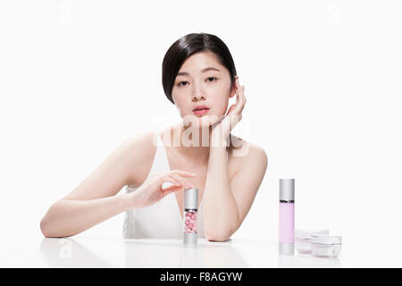 Young Asian woman touching a cosmetic container on the table with the other hand under her chin Stock Photo