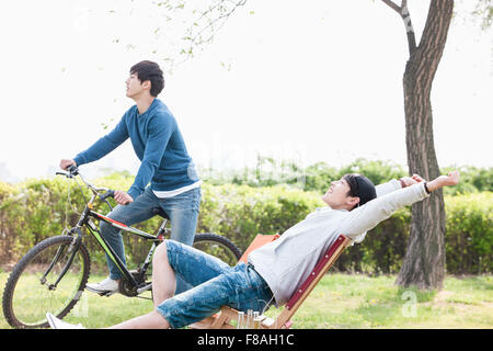 Young man on bike and the other young man stretching his arms sitting on a chair Stock Photo