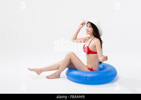 Asian woman in red bikini wear and a white hat sitting on a blue tube Stock Photo