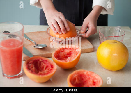 Grape fruit being squeezed with a juice extractor on a chopping board and grape fruit juice on the table Stock Photo
