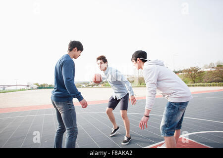 Three young men looking down and playing basketball at the court actively Stock Photo