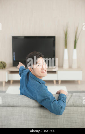 Portrait of young man looking back holding a TV remote control Stock Photo